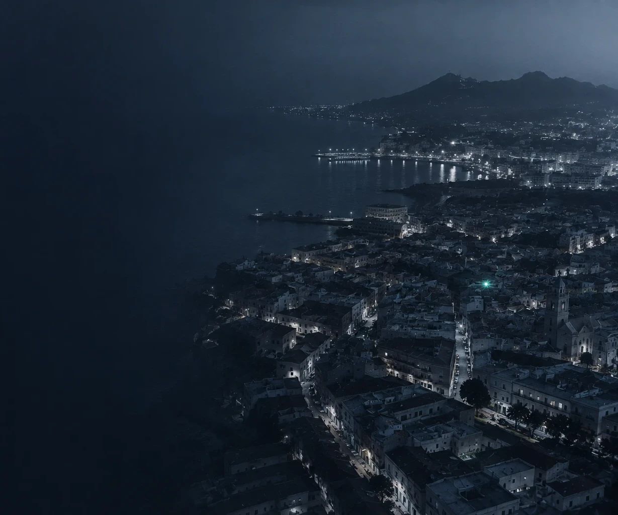 Vista aérea nocturna de una ciudad costera con un punto verde que destaca entre sus calles
